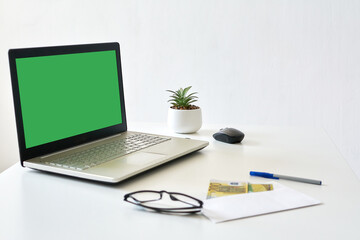 laptop with a blank green screen on a white wooden table against a white wall, mock up