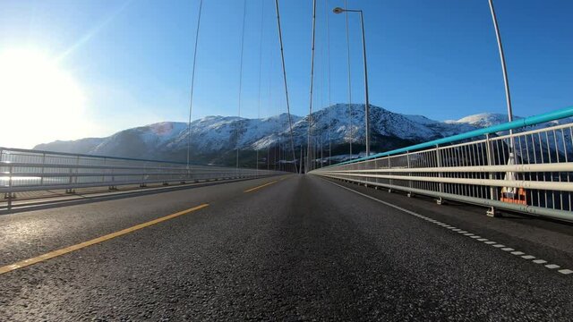 Driving over Hardanger bridge in beautiful sunshine with snow capped mountains in background - One of worlds longest suspension bridges