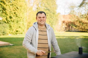 Fototapeta premium Man smiles and is happy while barbecuing in the garden. Man prepares the grill in the garden. 