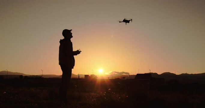 Sagoma di un ragazzo mentre pilota il drone al tramonto