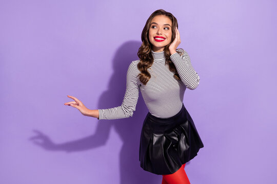 Photo of pretty shiny young lady dressed striped clothes looking pointing empty space dancing isolated purple color background
