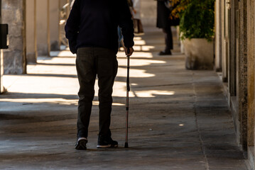 Old man walking alone with a cane along a street.
