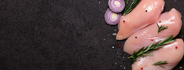 Raw chicken breast with spices and herbs on black stone background. Preparation for cooking, banner format