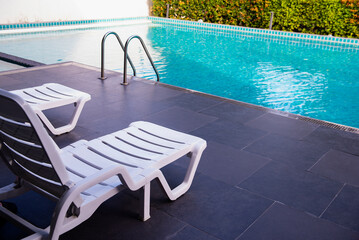 Fototapeta na wymiar White plastic lawn chair lounges on the blue poolside