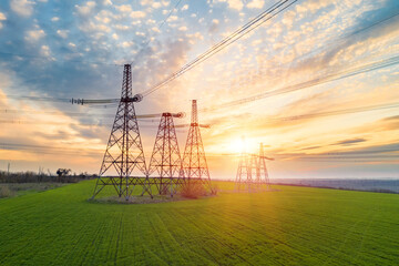 High voltage lines and power pylons in a flat and green agricultural landscape on a sunny day with...