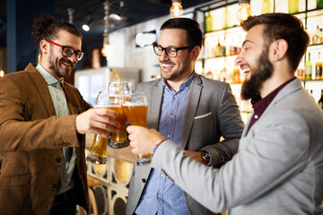 Leisure, friendship pub concept. Happy male friends drinking beer and clinking glasses at bar or pub