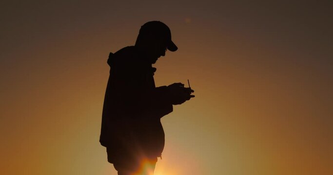 Sagoma di un ragazzo mentre pilota il drone al tramonto