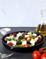 Greek salad with tomatoes, paprika, onions and feta cheese. Side view in a black plate on a white background