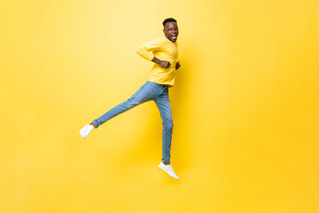 Fototapeta na wymiar Young happy excited African man jumping, raising one leg and clenching hands on isolated yellow studio background