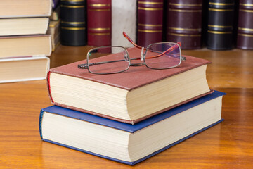 Eyeglasses on the two closed books against of other books