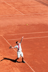 High angle view of young male tennis player performing service on orange clay court at start of match. Individual competition. Vertical sports background, banner, copy space