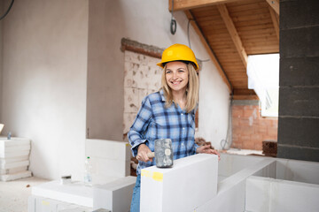 pretty young worker woman with yellow safety helmet works on construction site and puts up a wall indoor in a house and is happy
