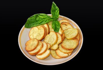 Spicy rusks with basil twig on saucer on black background