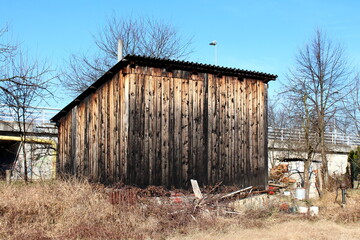Fototapeta na wymiar Dilapidated old wooden tool shed and storage area with large entrance doors built in abandoned suburban family house backyard surrounded with tall dry grass and backyard junk on warm sunny winter day
