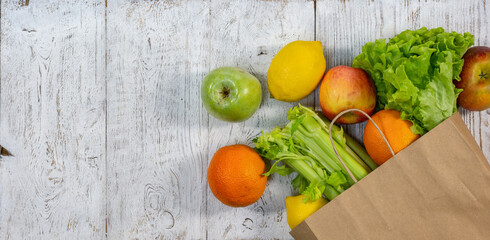 A background with fruits and vegetables peeking out of a paper bag on white-painted wooden boards.