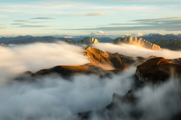 Mountains in fog at sunset in autumn. Landscape with alpine mountain valley, low clouds, forest, blue sky. Aerial view