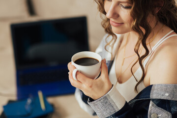 Close-up of woman drinking coffee while take break after work on the laptop. Woman sitting on a couch at home.