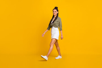 Full length profile side photo portrait of woman walking isolated on vivid yellow colored background