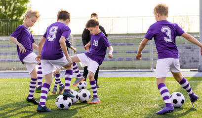 Happy young boys running and kicking the soccer ball on training. Group of school kids in purple...