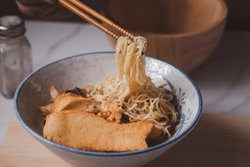 Chopsticks are holding noodles in a bowl.