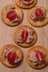 Obraz na płótnie Canvas Tuna crackers, bread decorated with tomatoes on a wooden cutting board Copy space