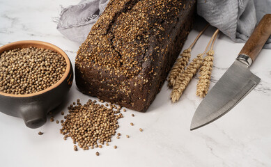Whole homemade black bread with cereal on a marble table with a knife and a towel