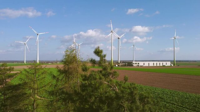Aerial view of large wind turbines with blades in field against the background of blue sky and white clouds. Alternative energy. Drone footage of wind farm generating green energy.