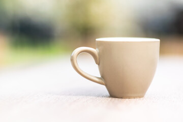 Little brown espresso cup on a wooden table with blurry garden background