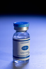 Covid-19 vaccine. Pandemic immunization. Coronavirus prevention. Flu inoculation. Dose vial glass bottle with label on defocused dark blue background.