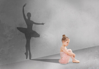 Cute little girl sitting on floor in dance studio, shadow of ballet dancer on grey wall, dreaming...