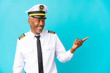 Airplane pilot senior man isolated on blue background pointing finger to the side and presenting a product