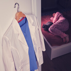 Tired doctor sleeps at home on a bed with a cat, white medical uniform on a hanger in the bedroom