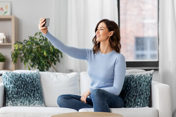 technology and people concept - happy smiling woman with smartphone and taking selfie sitting on sofa at home