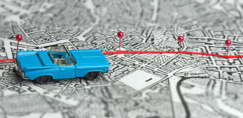 Concept. Following the route. A toy blue convertible is driving across the map. The direction is indicated by red safety pins. Finding a path, a goal, a road.