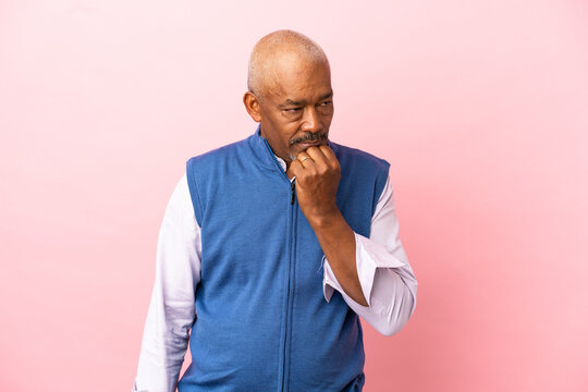 Cuban senior isolated on pink background having doubts