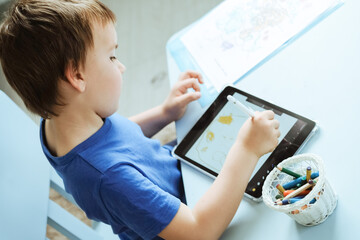 Cute boy in blue t shirt using digital tablet or computer for drawing his picture, using stylus . New technology art, online education