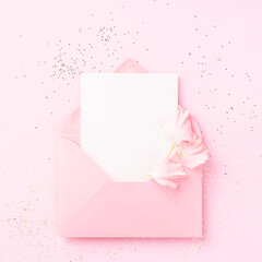 Blank white card in pink envelope with carnations petals on pink background with confetti.
