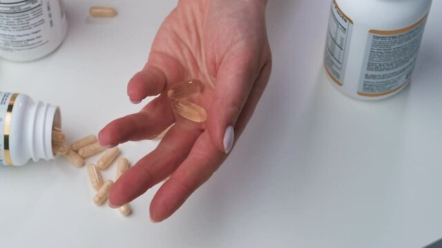 Slow motion. Female opens fist with pills, fish oil omega-3 on the white background. Close-up. 