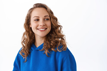 Portrait of blond happy woman look aside at promotional text, smiling satisfied, gazing at something beautiful, white background