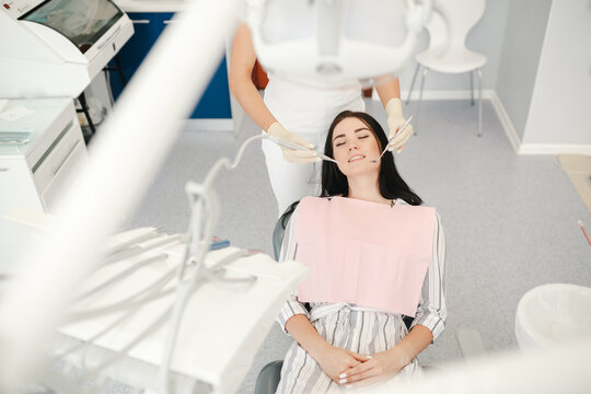 Image of pretty young woman sitting in dental chair at medical center while professional doctor fixing her teeth