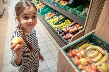 Little girl eats an apple from the counter of the store.