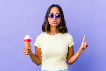 Young mixed race woman eating an ice cream showing number one with finger.