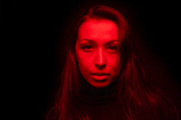 Young pretty woman looks at camera in contrast red light. Sensual female person posing in dark studio with red neon lightning. Portrait of beautiful sexy woman, art fashion beauty concept