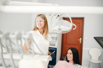 Fototapeta premium Young woman getting dental treatment. Young female doctor dentist look at female patient in the chair, explaining tretatment plan