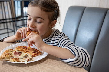 Little girl eating slices of appetizing pizza close up.