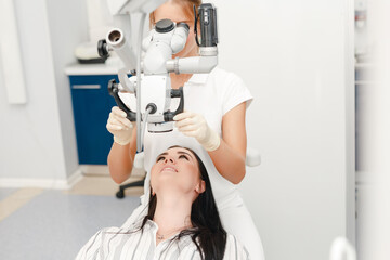A dentist is looking in a special microscope for dentist in a laboratory wit patient sit in the chair. Close-up of female dentistry at the workplace