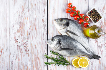 Fresh fish dorado on white wooden background with ingredients for cooking