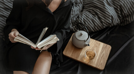 A woman is resting in bed with a book and tea.