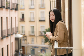 Fototapeta na wymiar lifestyle portrait of young beautiful and thoughtful Asian Korean woman at home or hotel balcony enjoying morning coffee looking to the street relaxed