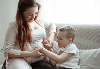 A young pregnant woman is sitting on the couch with her little son.